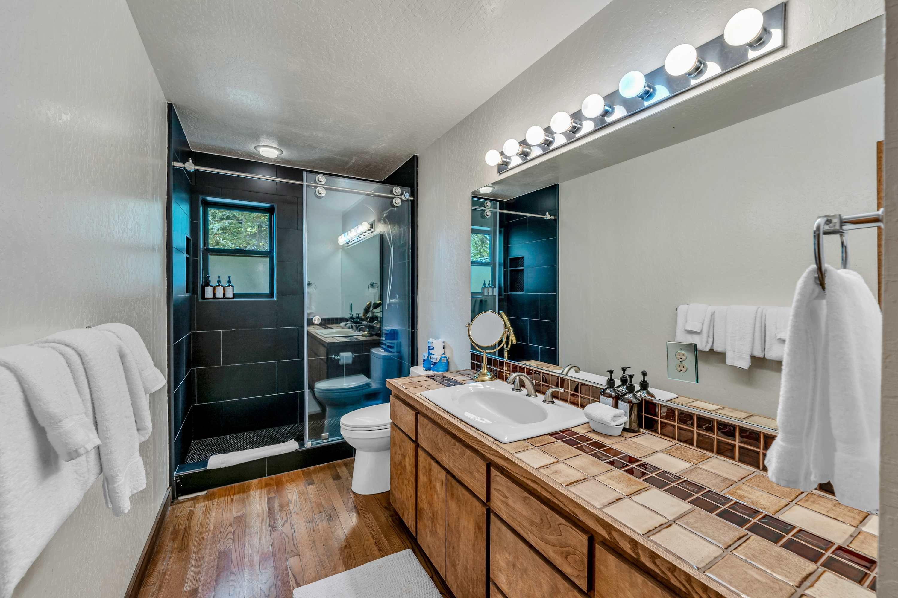 A modern bathroom with a glass shower enclosure, a large mirror, and a vanity with a tiled backsplash.