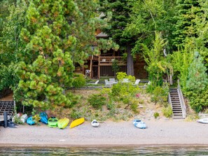 A cabin with a deck and chairs, surrounded by trees and a beach with kayaks. - Tahoe Waterfront Oasis | Deck & Lake Views/Access (Carnelian Bay)