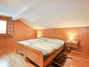 A bedroom with a wooden bunk bed, bedside tables with lamps, a window with curtains, and a wooden floor. - Weissmies Appartement/Fewo 5-Bettwohnung by Interhome (Saas-Grund)