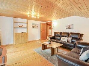 Ein Wohnzimmer mit Holzboden, einem braunen Ledersofa, einem Holztisch und einer Schrank mit Regalen.