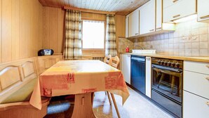 A compact kitchen with a dining table, a built-in oven, and a window with curtains. - Weissmies Appartement/Fewo 5-Bettwohnung by Interhome (Saas-Grund)