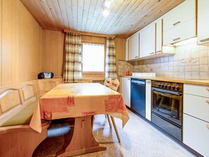 A compact kitchen with a dining table, a built-in oven, and a window with curtains. - Weissmies Appartement/Fewo 5-Bettwohnung by Interhome (Saas-Grund)
