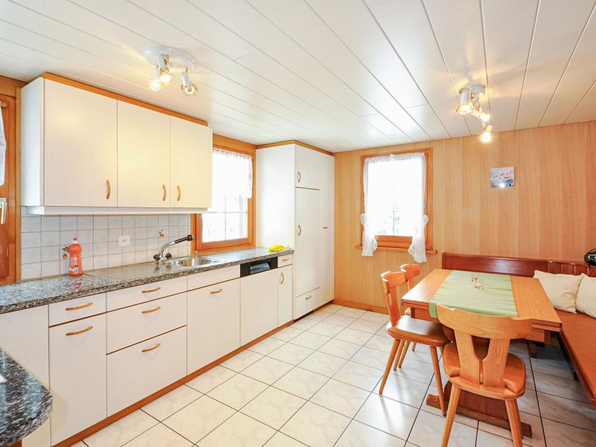 Een compacte keuken met witte kastjes, een granieten aanrecht en een eethoek met een houten tafel en stoelen.