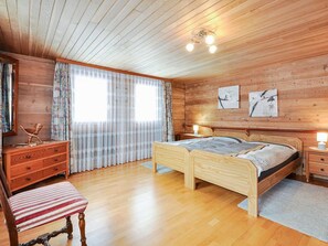 A wooden cabin bedroom with two single beds, a dresser, a chair, and a window with curtains. - Weissmies Appartement/Fewo 6-Bettwohnung by Interhome (Saas-Grund)