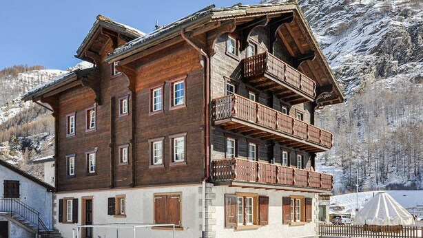 Un edificio in legno a più piani con balconi, sullo sfondo di una montagna innevata.