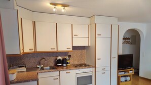 Una cucina compatta con mobili bianchi, un piano di lavoro in granito, un lavello, un fornello e un'area pranzo con tavolo e sedie in legno.