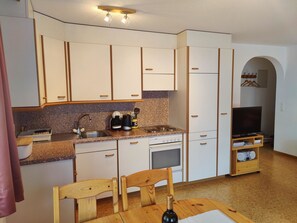 Eine kompakte Küche mit weißen Schränken, einer Arbeitsplatte aus Granit, einem Spülbecken, einem Herd und einem Essbereich mit einem Holztisch und Stühlen.