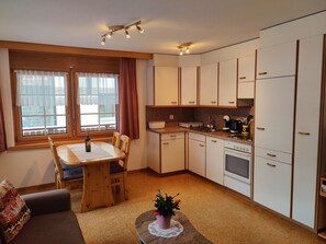 Une cuisine compacte comprenant un coin repas, des placards en bois, une cuisinière et une fenêtre avec des rideaux.