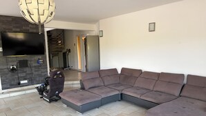 Ein modernes Wohnzimmer mit einer Eckcouch, einem Gaming-Sessel, einem Flachbildfernseher und einer integrierten Unterhaltungseinheit.