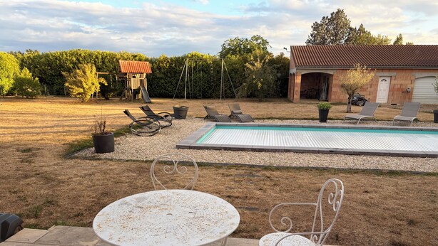 Ein Garten mit Swimmingpool, Terrassenmöbeln und einem Spielhäuschen.