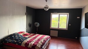 Ein Schlafzimmer mit einem Bett, einem Standventilator, einem Fenster und einer Deckenleuchte.