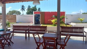 An outdoor patio with wooden furniture, a tiled floor, and a view of palm trees and a building in the background.