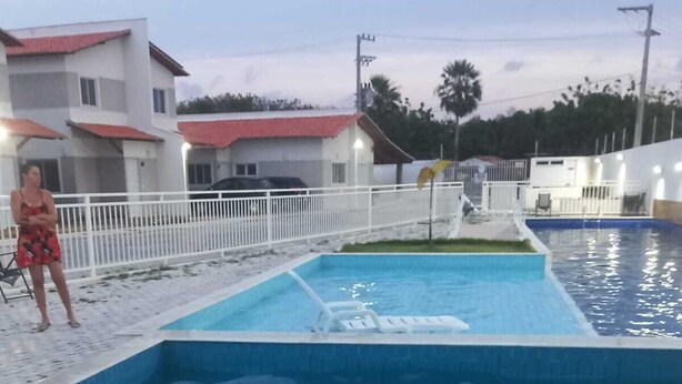 A swimming pool with a white fence, a person in a red swimsuit, and another in a white swimsuit.