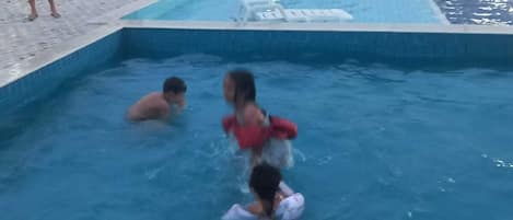 A swimming pool with a white fence, a person in a red swimsuit, and another in a white swimsuit.