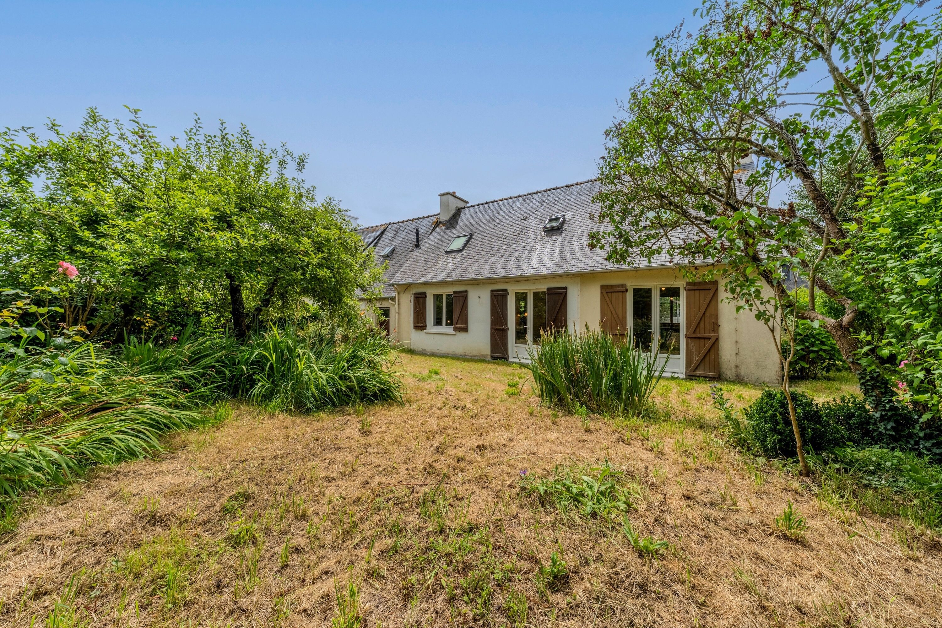 A house with a sloped roof, a front porch, and a garden with various plants and shrubs.
