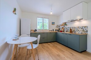 Una cocina moderna con comedor, que incluye un refrigerador blanco, una mesa de madera con sillas y un ventanal con persianas.