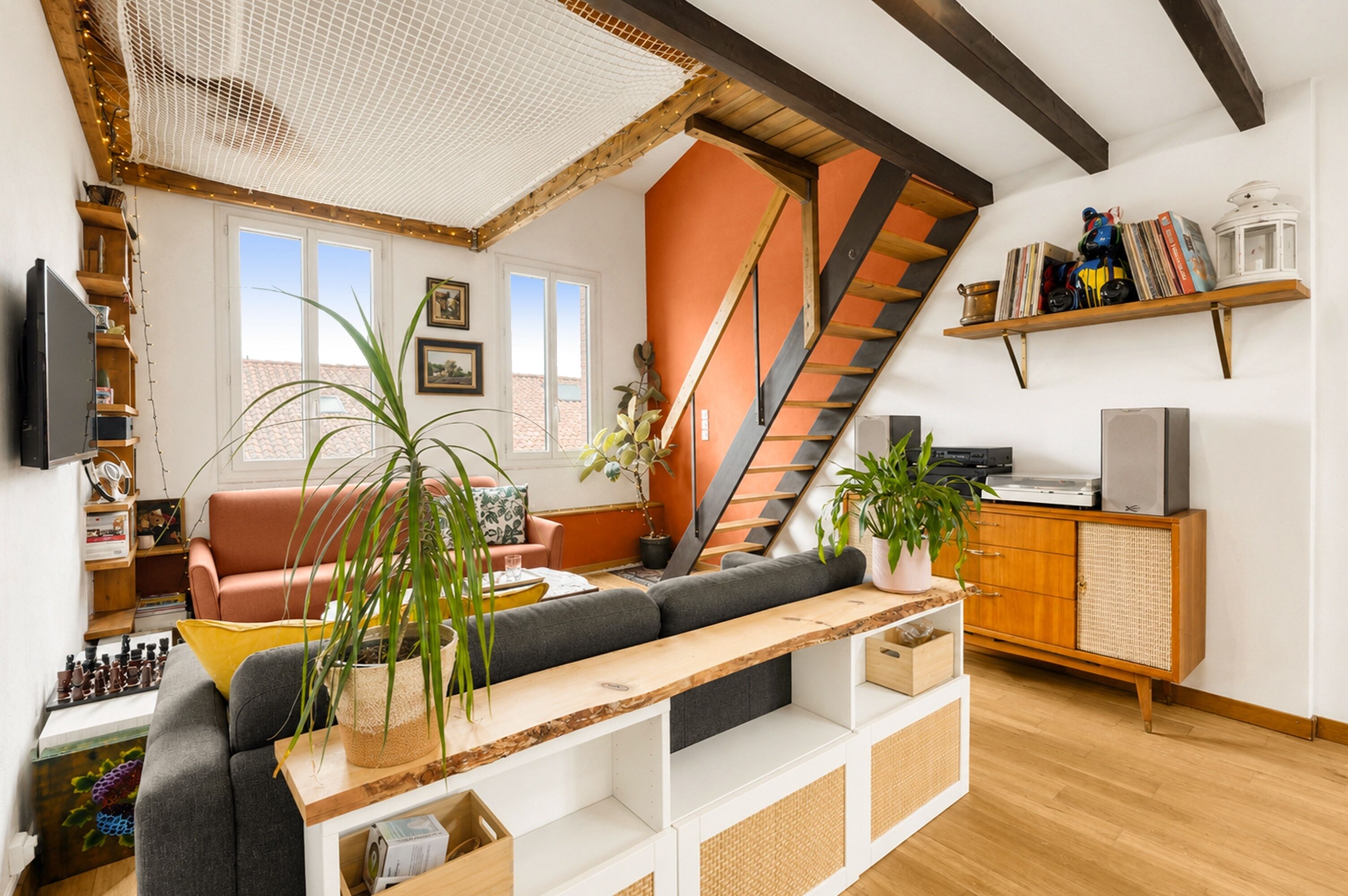 Un salon moderne avec un escalier, des poutres en bois, un canapé, une table basse et une bibliothèque.