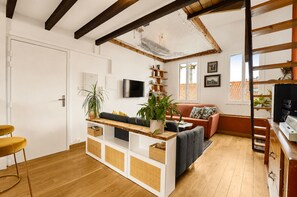 Ein modernes Wohnzimmer mit Holzboden, einer Couch, einem Couchtisch und einem an der Wand befestigten Fernseher.