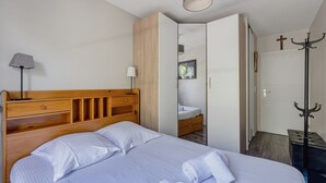 A bedroom with a wooden headboard, a bed with white linens, a bedside lamp, a wardrobe, a coat rack, and a door with a cross. - Les Terrasses de Michelle - Dune du Pilat à 15min (La Teste-de-Buch)