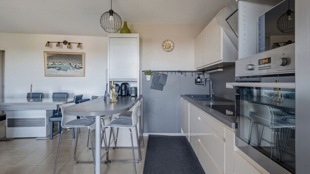 A modern kitchen with a central island, stainless steel appliances, and a dining area with chairs. - Les Terrasses de Michelle - Dune du Pilat à 15min (La Teste-de-Buch)