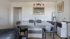 A dining area with a table, chairs, a painting, and a heater. - Les Terrasses de Michelle - Dune du Pilat à 15min (La Teste-de-Buch)