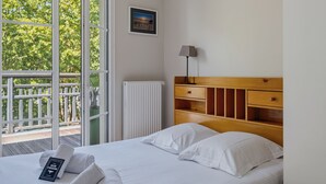 A hotel room with a bed, a bedside lamp, a radiator, a picture on the wall, and a balcony with a view of trees. - Les Terrasses de Michelle - Dune du Pilat à 15min (La Teste-de-Buch)