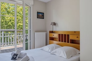 Ein Hotelzimmer mit einem Bett, einer Nachttischlampe, einer Heizung, einem Bild an der Wand und einem Balkon mit Blick auf Bäume.