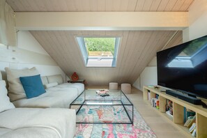 A modern loft bedroom with a sloped ceiling, a large window, a sofa, a coffee table, a TV, and bookshelves. - Villa Alba - Vue panoramique sur lac et montagnes (Sévrier)