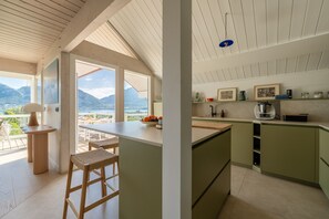 A kitchen with a view of mountains, a dining area with a table and chairs, and a bar stool. - Villa Alba - Vue panoramique sur lac et montagnes (Sévrier)