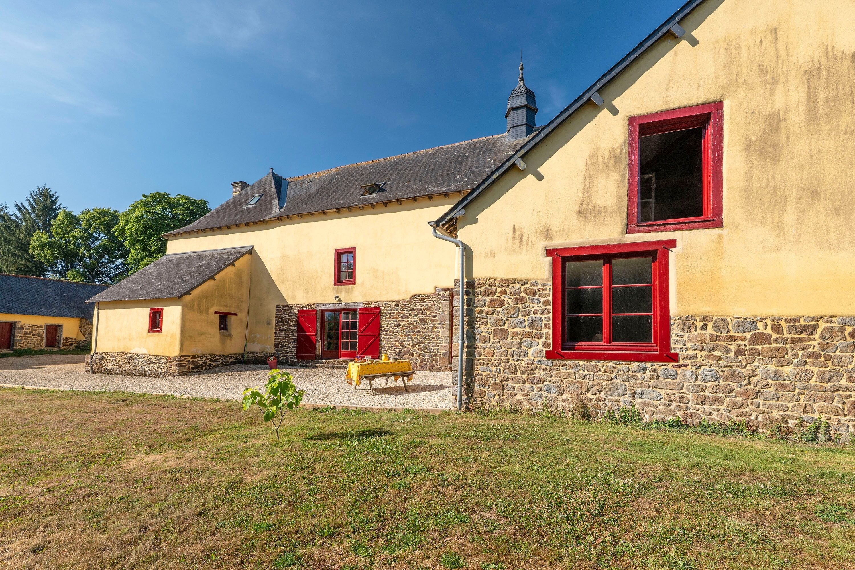 Un bâtiment traditionnel en pierre et en crépi, avec des encadrements de fenêtres rouges et un toit en pente.