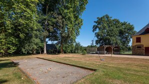 Une cour comprenant un terrain de croquet, un espace de repos abrité et un bâtiment dont les fondations sont en pierre.