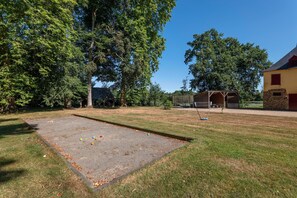 Ein Innenhof mit einem Krocketplatz, einer überdachten Sitzgelegenheit und einem Gebäude mit steinernen Fundamenten.