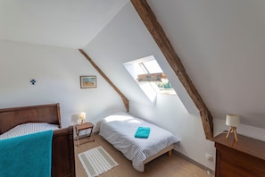 Ein Schlafzimmer mit schrägen Wänden, einem Bett, einem Nachttisch mit Lampe, einem kleinen Fenster und einem Bild an der Wand.