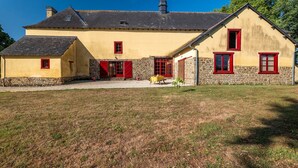 Un bâtiment à deux étages, doté de fondations en pierre et d’une façade jaune, avec des fenêtres à cadre rouge et une petite structure en forme de tour sur le toit.