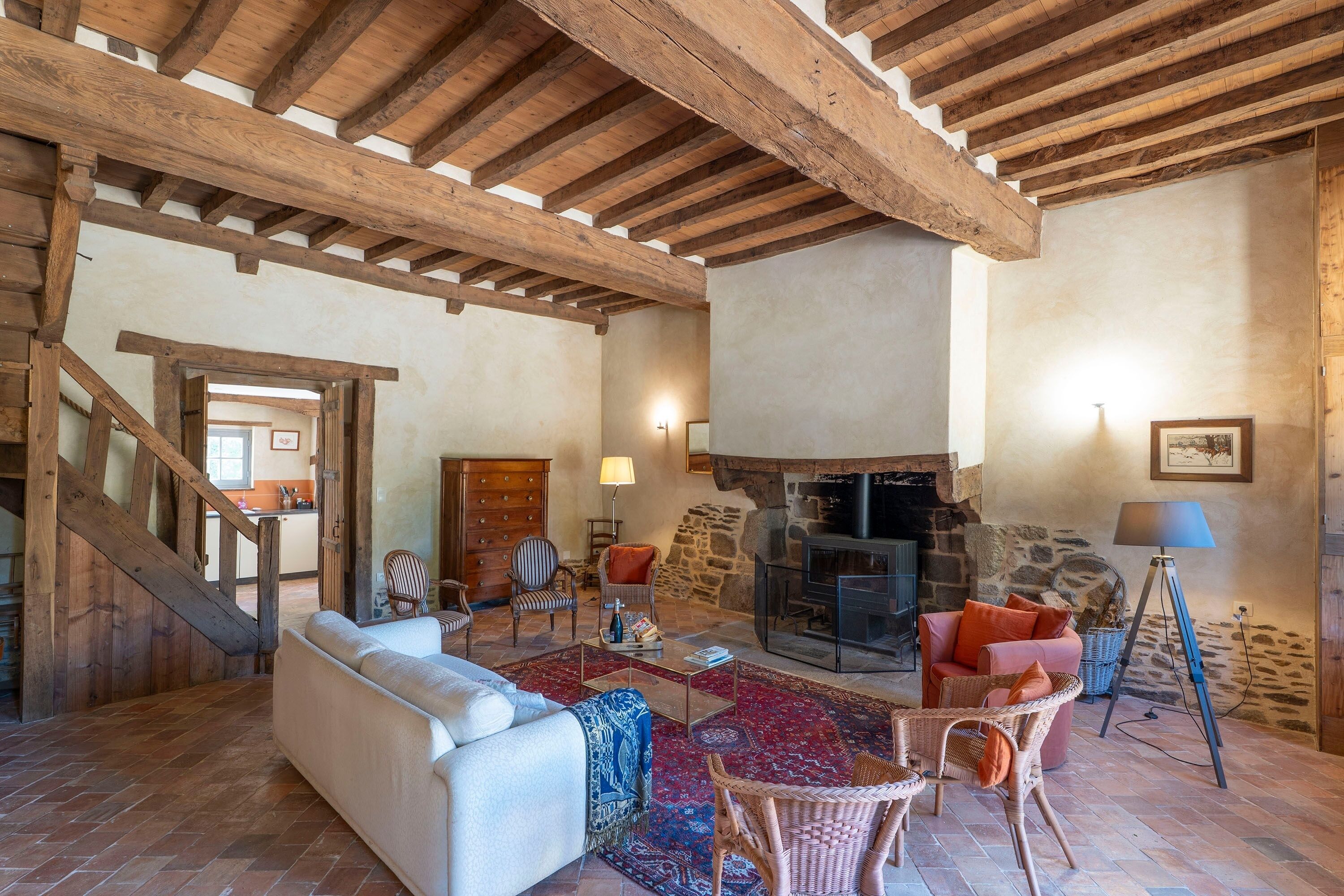 A rustic interior with exposed wooden beams, a stone fireplace, a sofa, and wicker furniture.