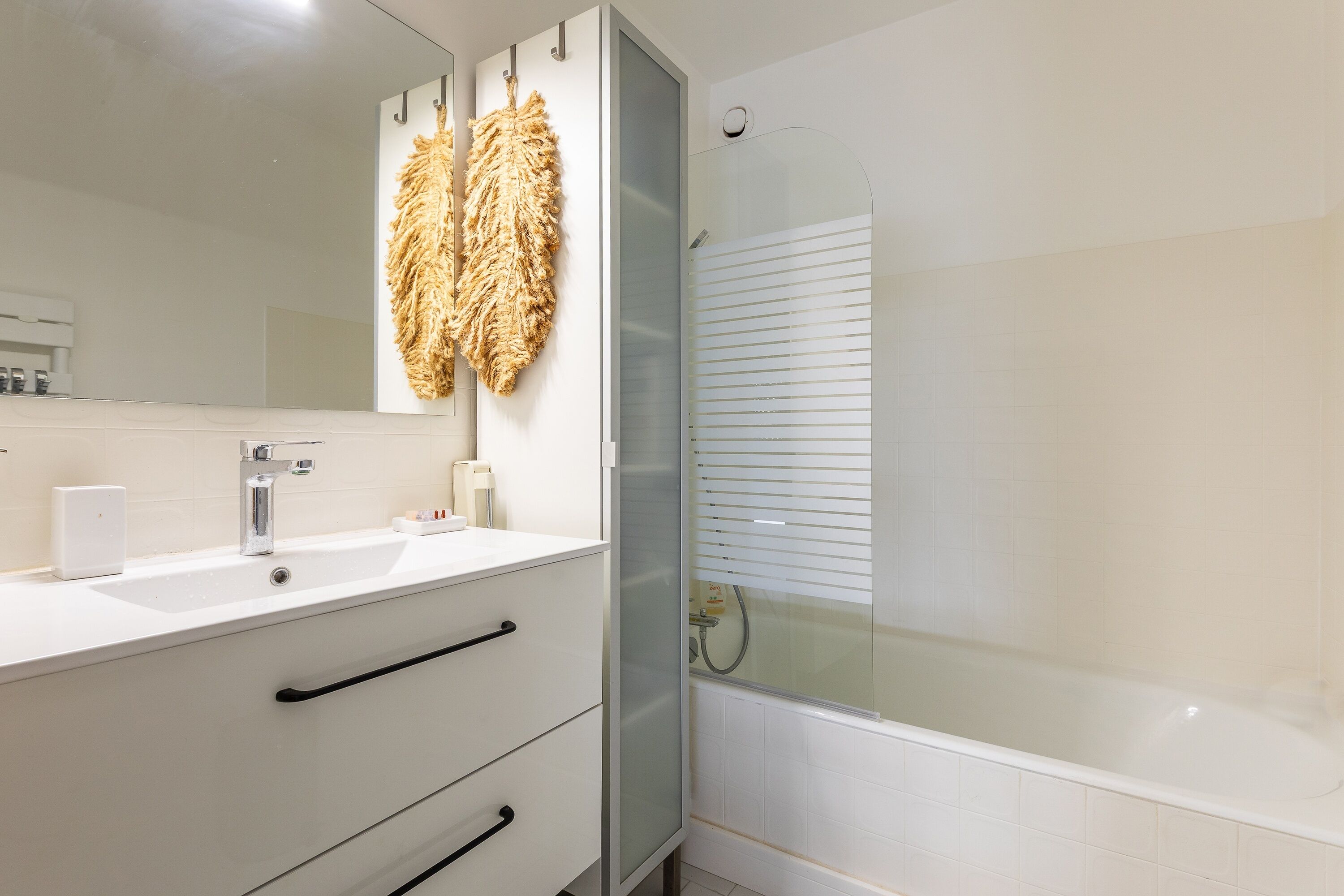 Ein Badezimmer mit weißem Waschbecken, einem Spiegel, einem Handtuchhalter mit großem Handtuch, einer Dusche mit Milchglas-Türen und einer Toilette.