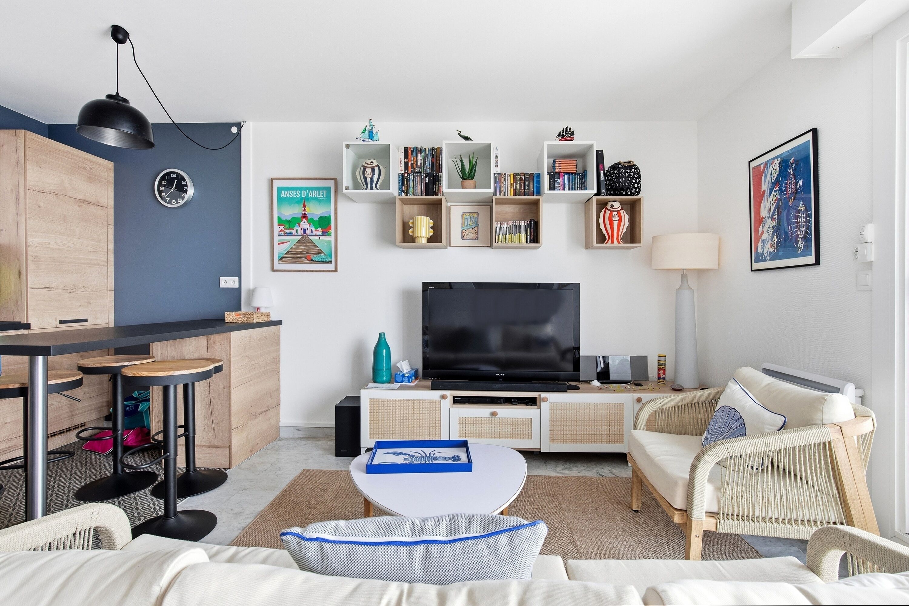 En moderne stue med et fladskærms-TV, et spiseområde med en barstol og et siddeområde med en sofa og lænestole.