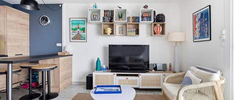 En moderne stue med et fladskærms-TV, et spiseområde med en barstol og et siddeområde med en sofa og lænestole.