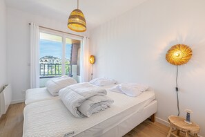 Ein Schlafzimmer mit einem Bett, zwei Wandlampen, einem Fenster mit Vorhängen und Blick auf Gebäude.