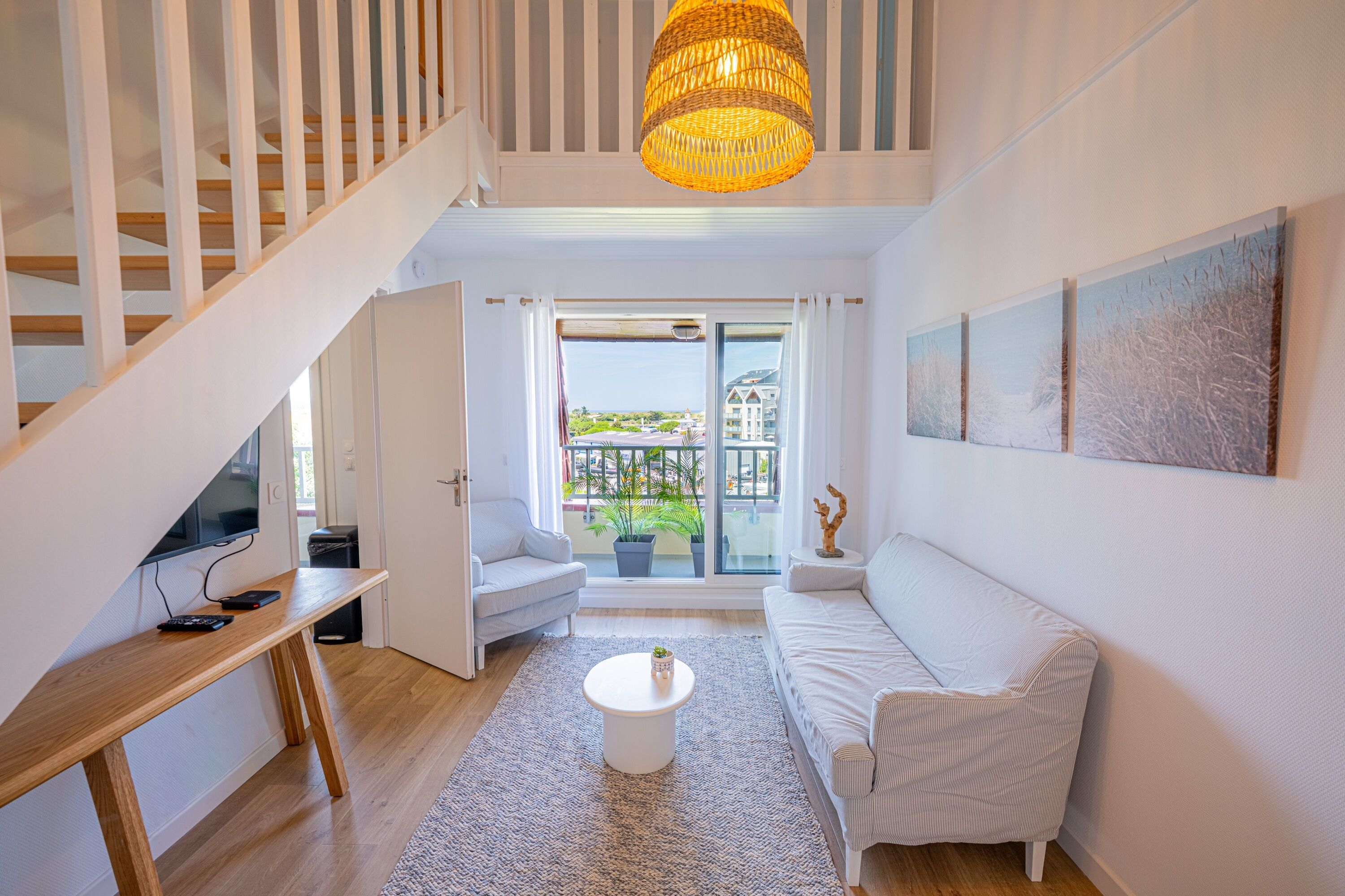 Un salon moderne avec un escalier, un canapé, une table basse et une vue à travers une porte vitrée.
