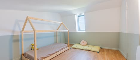Una habitación con una cama litera de madera, un ventanal pequeño y un cojín verde en el suelo.