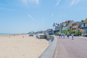 Eine Uferpromenade mit Sandstrand, einer gewundenen Steinmauer und einer Reihe von Gebäuden mit Fahnen.