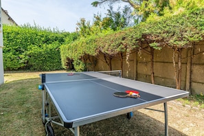Ett utomhusbordtennisbord med nät, två racketar och två bollar.