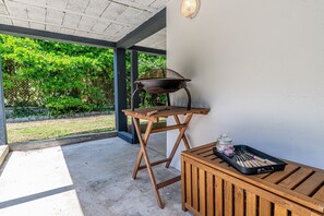 Een terras buiten met een barbecue, een houten tafel en een zwarte dienblad met bestek.