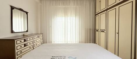 A hotel room with a large bed, a dresser, a mirror, and a wardrobe.