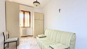 Una habitación con un sofá verde, una silla, un radiador y una ventana con cortinas.