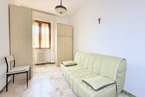 Quarto com sofá verde, uma cadeira, radiador e janela com cortinas.