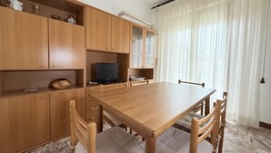 Un comedor con mesa y sillas de madera, televisor y armarios con puertas de vidrio.