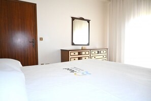 A hotel room with a wooden door, a dresser with multiple drawers, a large mirror, and a bed with a logo on the bedspread. - SE274 – Marotta, spacious four-room apartment with parking space (Marotta)