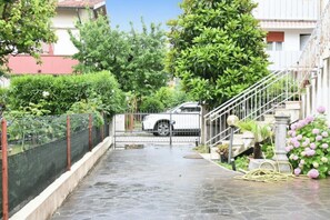 Uma entrada com portão leva a um edifício onde um carro branco está estacionado.